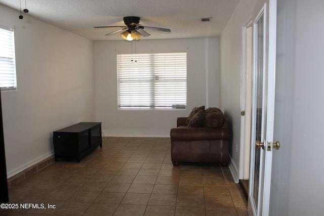 living area with visible vents, a textured ceiling, tile patterned flooring, baseboards, and ceiling fan