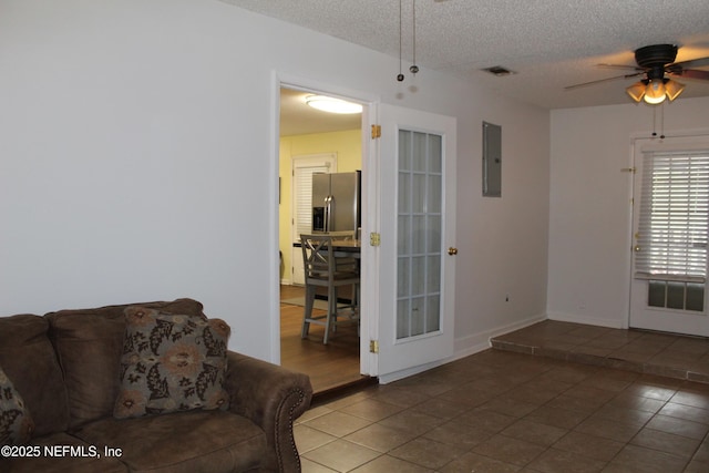 living room featuring electric panel, visible vents, a textured ceiling, and a ceiling fan