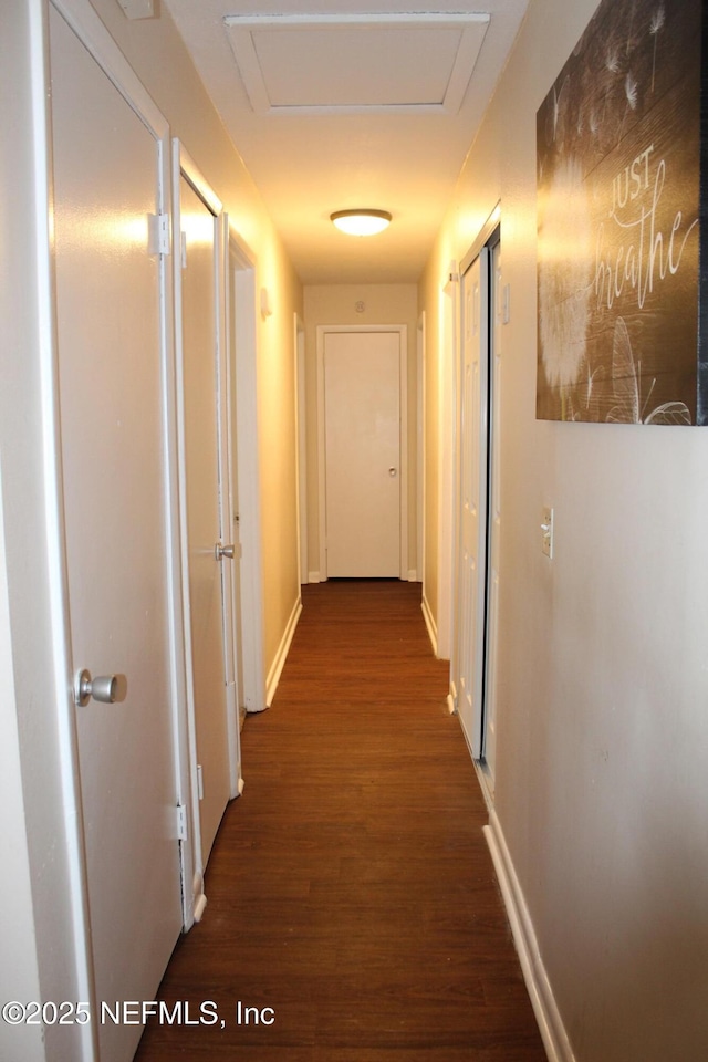 corridor featuring attic access, dark wood-type flooring, and baseboards