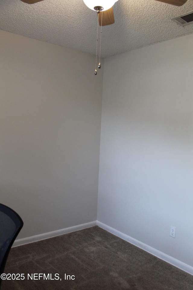 spare room featuring visible vents, dark carpet, a textured ceiling, and baseboards