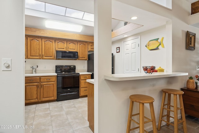 kitchen featuring light tile patterned floors, light countertops, brown cabinetry, black appliances, and a kitchen breakfast bar