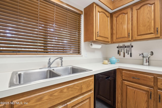 kitchen featuring brown cabinets, black dishwasher, light countertops, and a sink