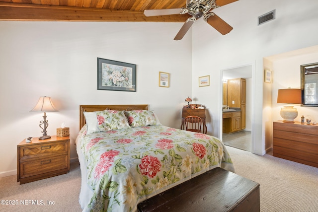 bedroom featuring light carpet, baseboards, visible vents, ensuite bath, and beamed ceiling