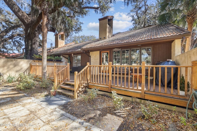 back of property with a tiled roof, a chimney, and a wooden deck