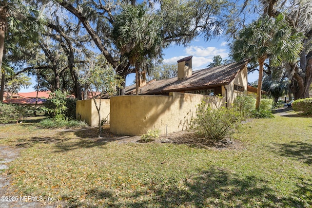 view of home's exterior with fence, a lawn, a chimney, and stucco siding