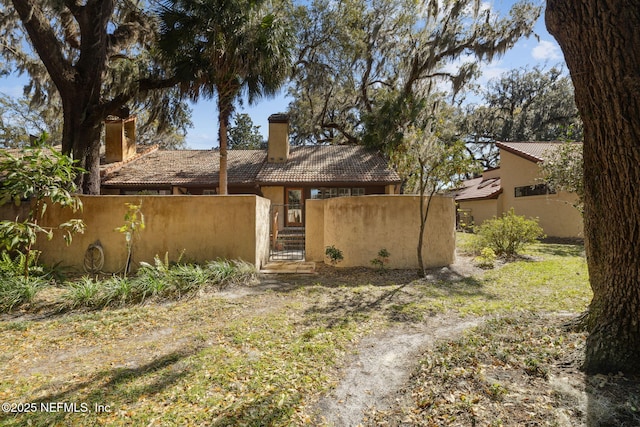 view of front of house with a fenced front yard, a chimney, stucco siding, a gate, and a tiled roof