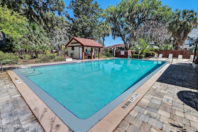 community pool featuring a fenced backyard, a patio, and an outbuilding