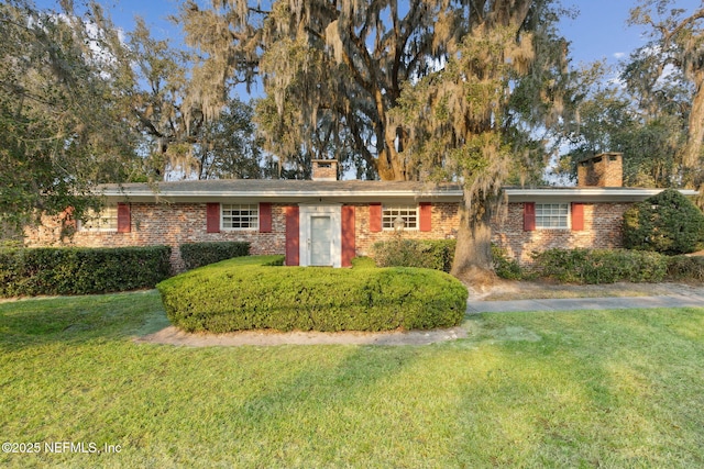 ranch-style home with brick siding, a chimney, and a front yard