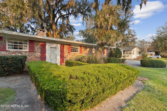 ranch-style house with a front yard, brick siding, and a chimney