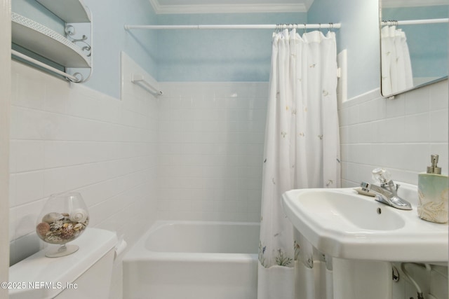 bathroom featuring tile walls, toilet, ornamental molding, shower / bathtub combination with curtain, and a sink