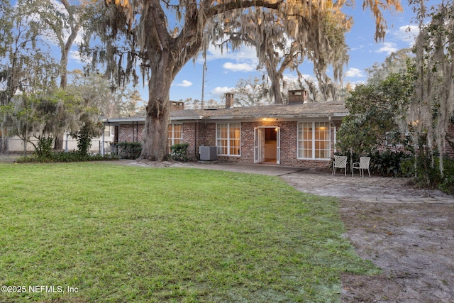 rear view of property featuring a chimney, cooling unit, a yard, a patio area, and brick siding