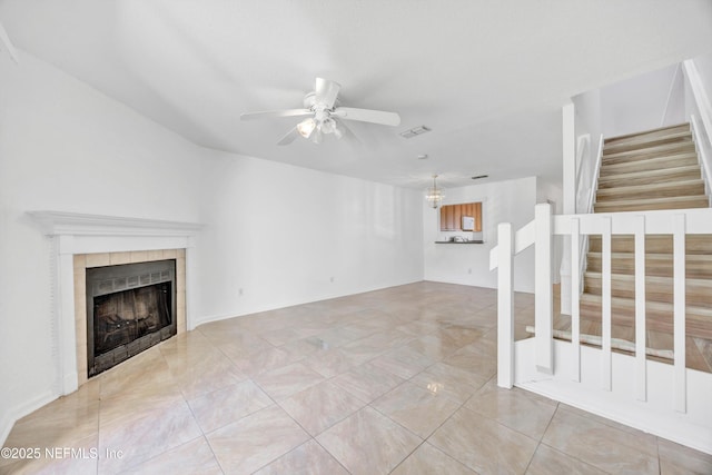 unfurnished living room with stairs, a ceiling fan, visible vents, and a tile fireplace