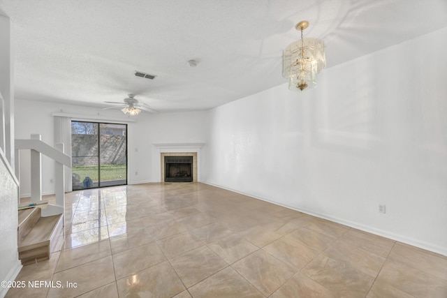 unfurnished living room with visible vents, a tile fireplace, tile patterned flooring, a textured ceiling, and ceiling fan with notable chandelier