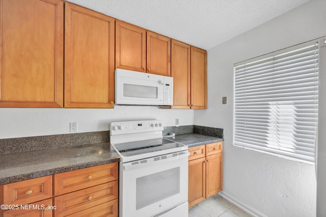 kitchen with white appliances, light tile patterned floors, a textured ceiling, dark countertops, and brown cabinets