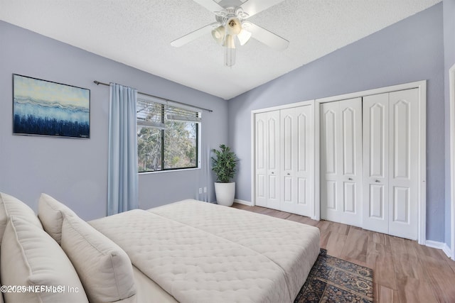 bedroom featuring multiple closets, lofted ceiling, light wood-style floors, a textured ceiling, and a ceiling fan