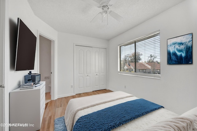 bedroom featuring light wood-style flooring, a textured ceiling, a closet, baseboards, and ceiling fan