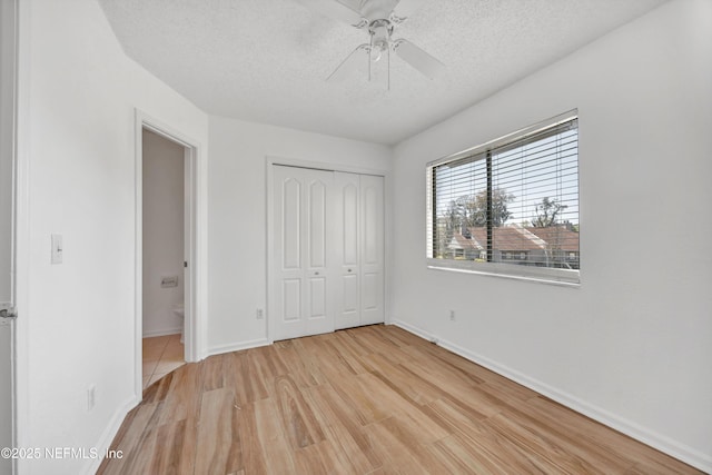 unfurnished bedroom featuring a textured ceiling, a closet, light wood-style floors, baseboards, and ceiling fan