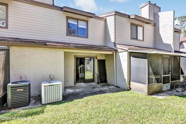 rear view of house featuring central air condition unit, a yard, a sunroom, and stucco siding