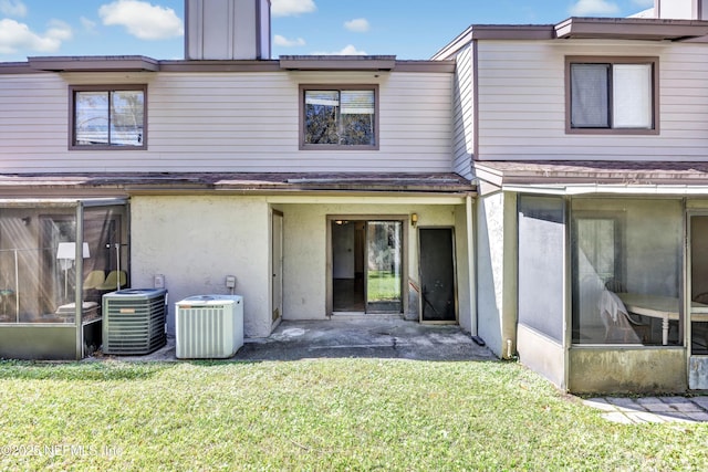 rear view of property with cooling unit, a lawn, a sunroom, and stucco siding