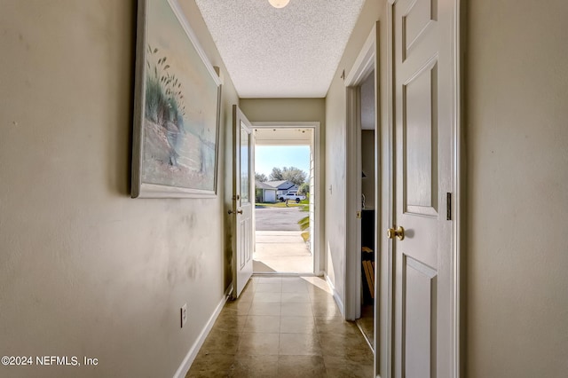 corridor featuring a textured ceiling, tile patterned flooring, and baseboards