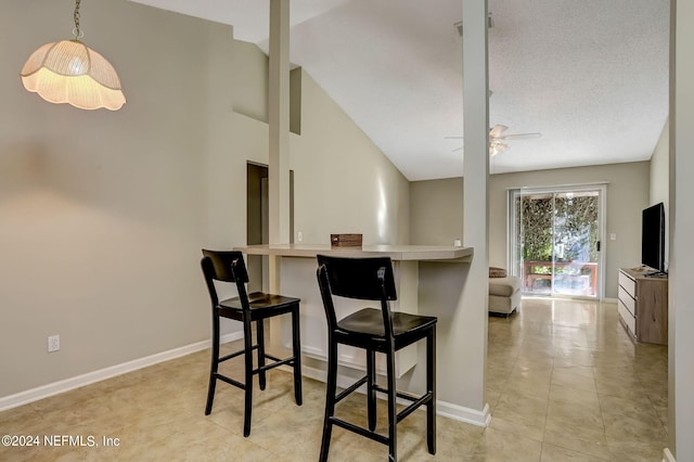 kitchen with ceiling fan, a breakfast bar area, lofted ceiling, and baseboards