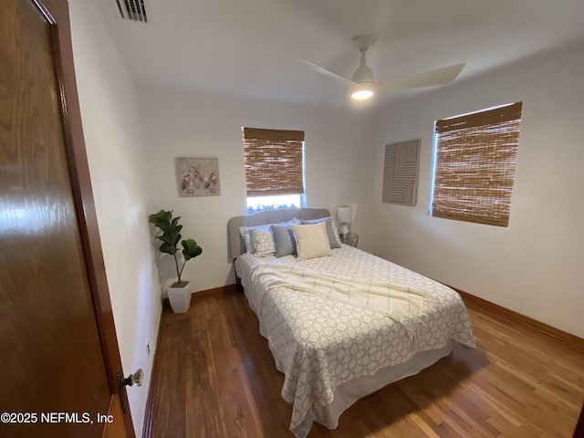 bedroom featuring a ceiling fan, wood finished floors, visible vents, and baseboards