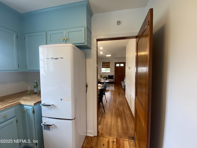 kitchen with blue cabinetry, visible vents, wood finished floors, and freestanding refrigerator