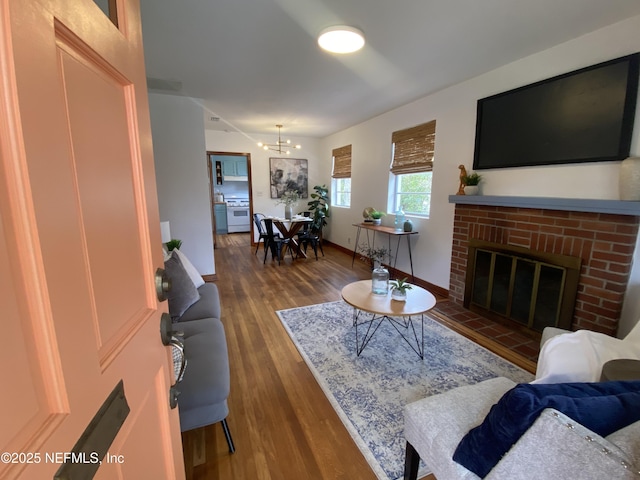 living area with a chandelier, a fireplace, baseboards, and wood finished floors