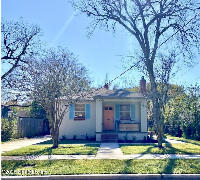 bungalow-style house featuring a porch, fence, a front lawn, and stucco siding