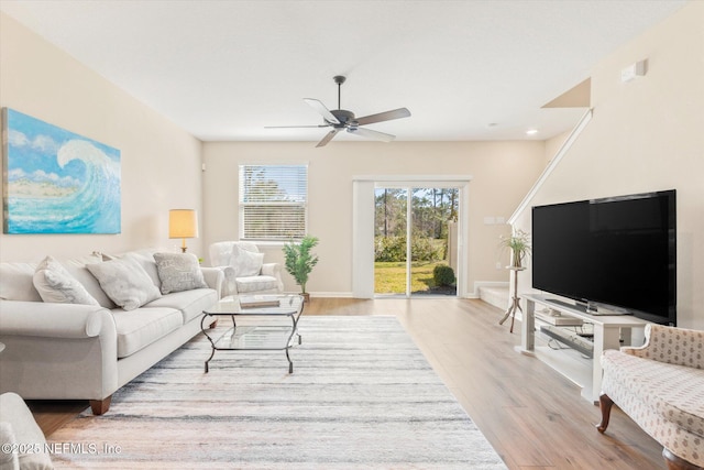 living area with light wood-type flooring, a ceiling fan, and baseboards