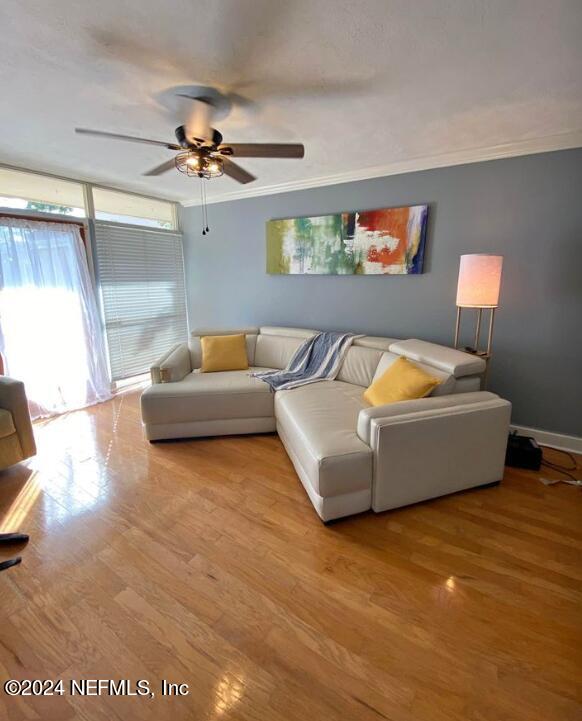 living room with baseboards, wood finished floors, a ceiling fan, and crown molding