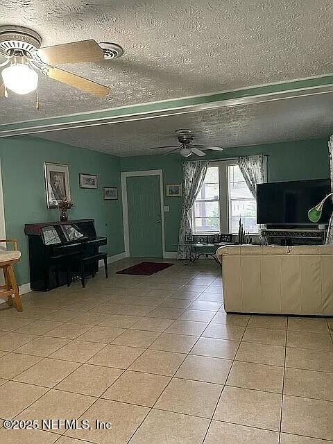 living area with light tile patterned floors, a textured ceiling, baseboards, and a ceiling fan