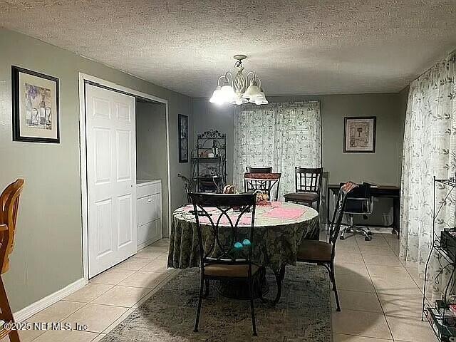 dining area with light tile patterned flooring, a notable chandelier, a textured ceiling, and baseboards