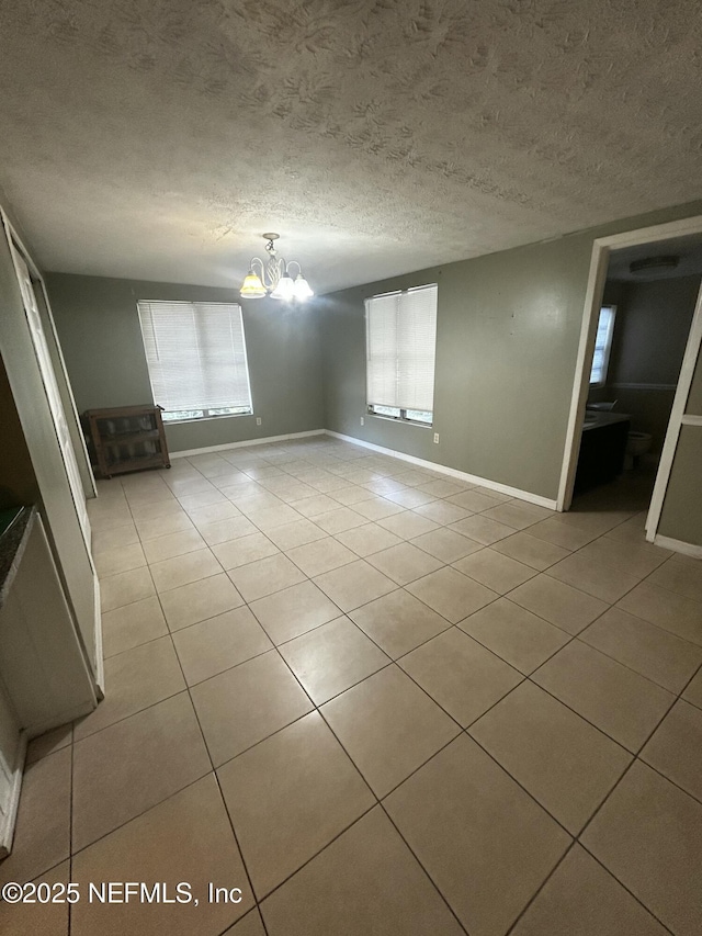 spare room featuring light tile patterned floors, a textured ceiling, and a notable chandelier