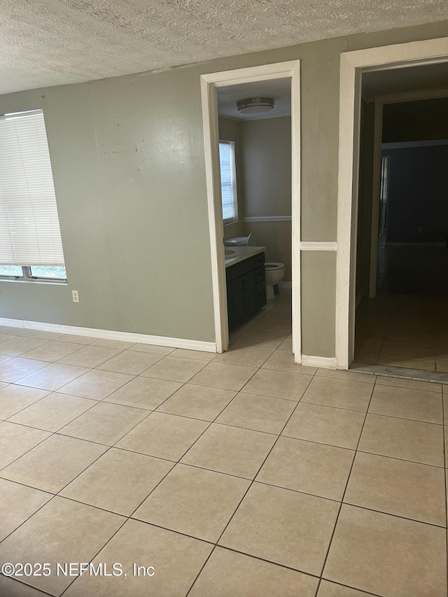 unfurnished room featuring light tile patterned floors, a textured ceiling, and baseboards