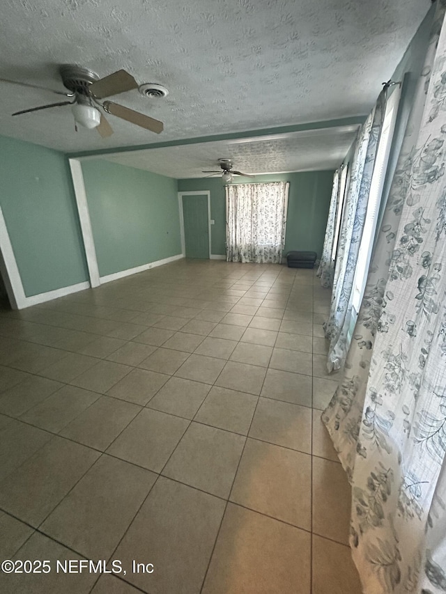 empty room featuring baseboards, visible vents, a ceiling fan, tile patterned floors, and a textured ceiling