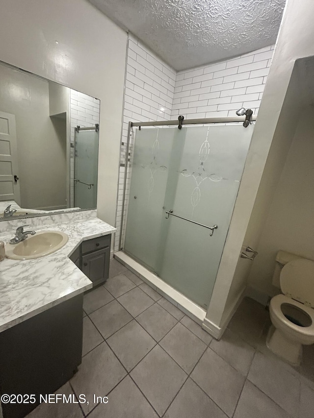 bathroom featuring a stall shower, toilet, tile patterned flooring, a textured ceiling, and vanity