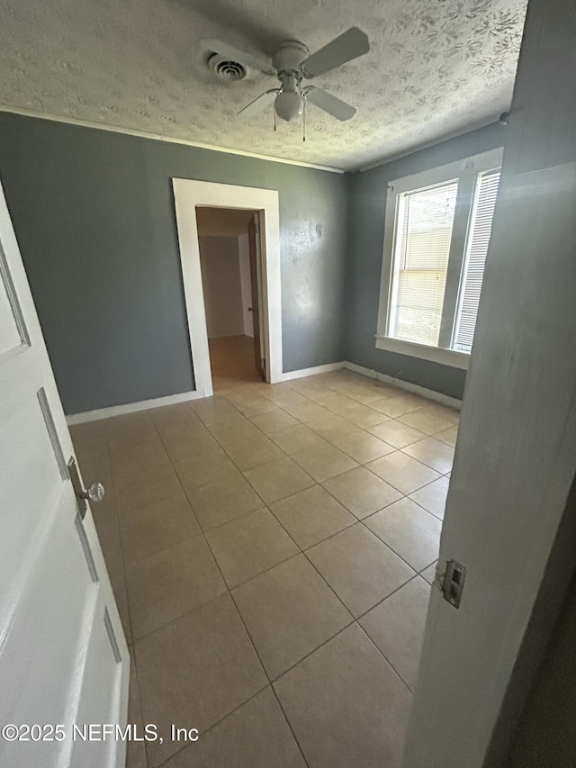 tiled spare room featuring baseboards, visible vents, a ceiling fan, and a textured ceiling