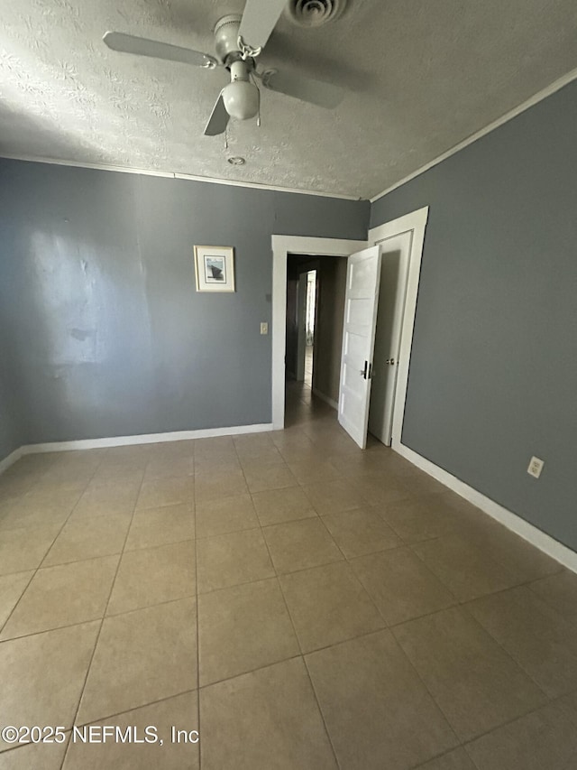 empty room featuring a textured ceiling, baseboards, crown molding, and tile patterned floors