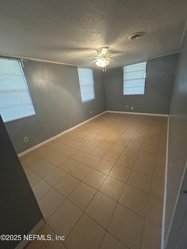 empty room with a textured ceiling, ceiling fan, a wealth of natural light, and tile patterned floors