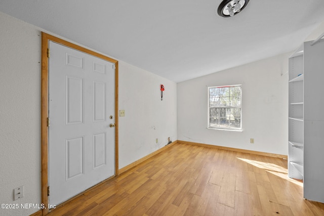 spare room with light wood-type flooring, lofted ceiling, and baseboards