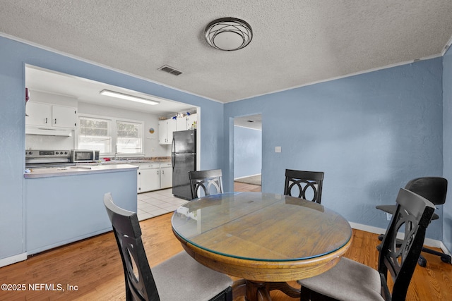 dining room with baseboards, visible vents, light wood-style flooring, ornamental molding, and a textured ceiling