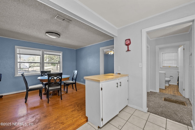 kitchen featuring visible vents, a peninsula, a textured ceiling, crown molding, and white cabinetry