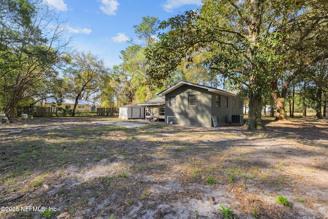 rear view of property with a storage unit, an outdoor structure, cooling unit, and fence