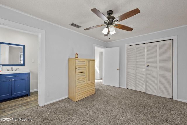 unfurnished bedroom with a textured ceiling, visible vents, a closet, carpet, and crown molding