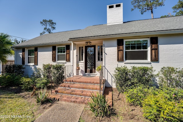 ranch-style house with roof with shingles, a chimney, and brick siding