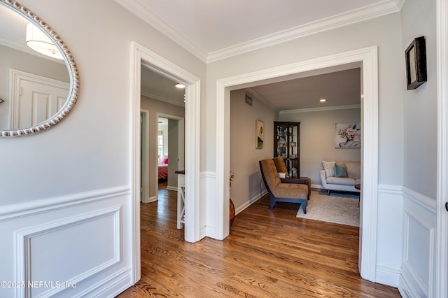 hallway featuring ornamental molding, wainscoting, visible vents, and light wood finished floors