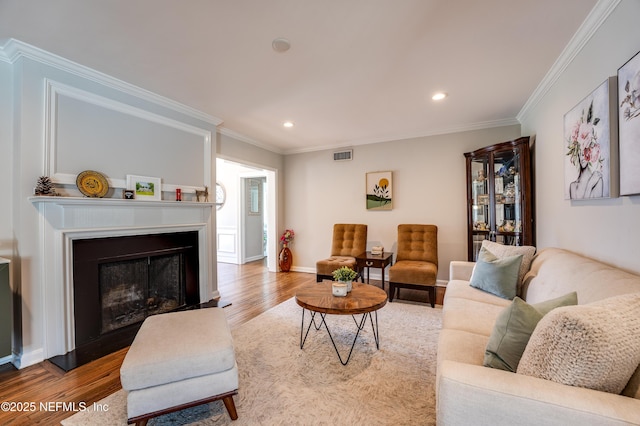 living room featuring visible vents, crown molding, a fireplace, and wood finished floors