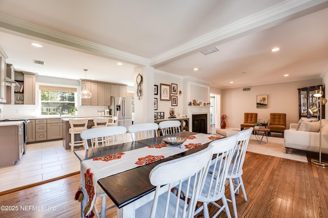 dining room featuring ornamental molding, light wood-type flooring, visible vents, and a fireplace