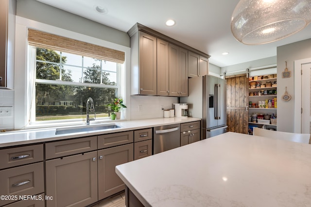 kitchen with appliances with stainless steel finishes, gray cabinets, a sink, and a barn door